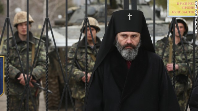 An Orthdox clergyman stands at the gate of a Ukrainian military base that was surrounded by several hundred Russian-speaking soldiers, as Ukrainian soldiers stand just inside the gate in Crimea on March 2.